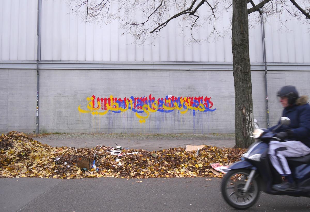 Image: "Unterwegs / On the Way" by Ella Ponizovsky Bergelson (2019, wall paint on concrete, Neukölln, Berlin). Part of a series of wall-writings created by Ella Ponizovsky Bergelson in 2018 and 2019 in many public places in Berlin. The multilingual text reads in German: 'Immer noch unterwegs', in Yiddish: 'נאך אונטערוועגן', and in Arabic: 'مازلت في الطريق', which translates into English: 'still on the way'.