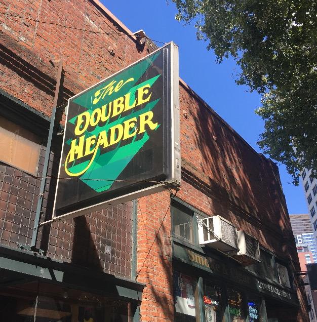 A sign for the Double Header bar hangs on a brick building in Pioneer square.