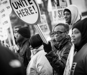 Black and white photo of protesters at a Black Lives Matter protest in Baltimore, Maryland. Protester in the middle holds a sign that reads, "Unite Here!"