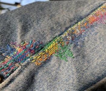 close up of a blue denim seam stitched with rainbow threads