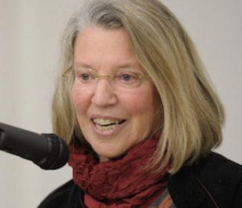 Close-up image of Nancy Fraser speaking into a microphone while wearing glasses and a red scarf.
