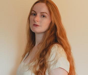 Caitlin looking sideways at the camera. She has long red hair and is wearing a white t-shirt