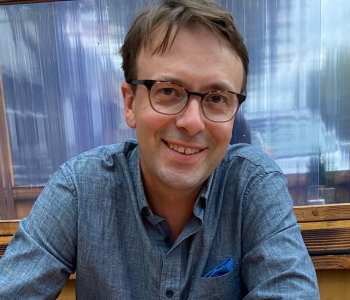 A close-up image of Jesse Oak Taylor wearing a blue shirt and glasses.