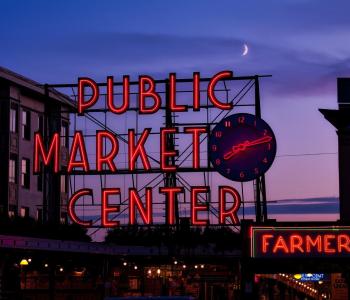 The signage for Pike Place Market illuminated against the sky at dusk.