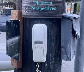 Various technologies like a landline phone and an iPad are nailed to a telephone pole. On the telephone pole, there is a sign that reads "Platform Perspectives"