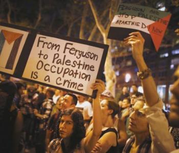 Protesters holding signs with the Palestinian flag that read "From Ferguson to Palestine, occupation is a crime" and "FERGUSON AND PALESTINE, STOP APARTHEID NOW"