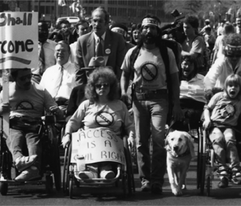 A photo of a group of protestors holding signs, many of them in wheelchairs.