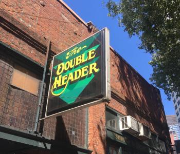 A sign for the Double Header bar hangs on a brick building in Pioneer square.