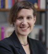 Mika Ahuvia in suit jacket smiling with bookcase in background