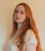 Caitlin looking sideways at the camera. She has long red hair and is wearing a white t-shirt