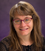 Portrait of Lynn Thomas wearing glasses and sitting in front of a purple wall.