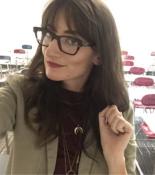 Photo of Alexandra Meany looking to the left while wearing glasses and a tan jacket